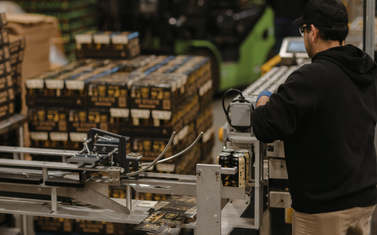 man working production line with stacked boxes of beer