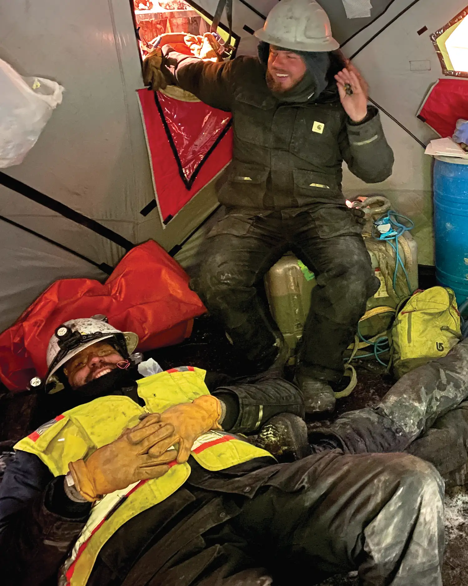 two construction crew workers relaxing in a tent while wearing utility clothing and work gear