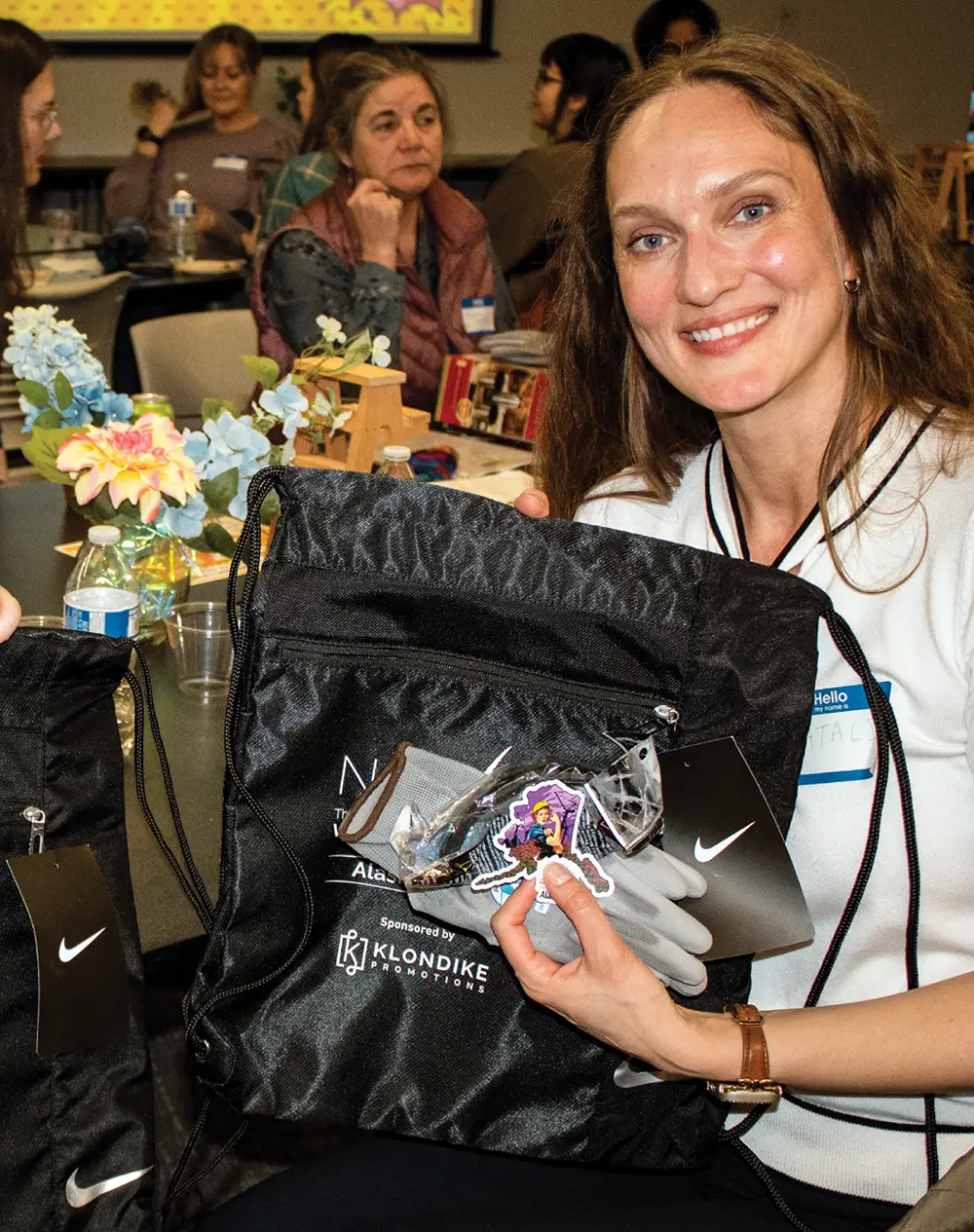 A woman smiling, holding a black Nike drawstring bag with gloves and stickers.