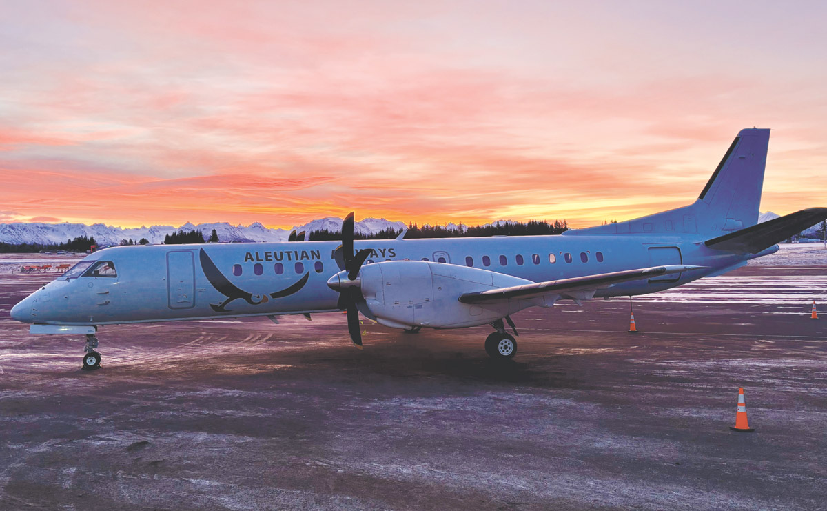 A regional airplane with "ALEUTIAN AIRWAYS" on its side, parked on a runway during a colorful sunset.
