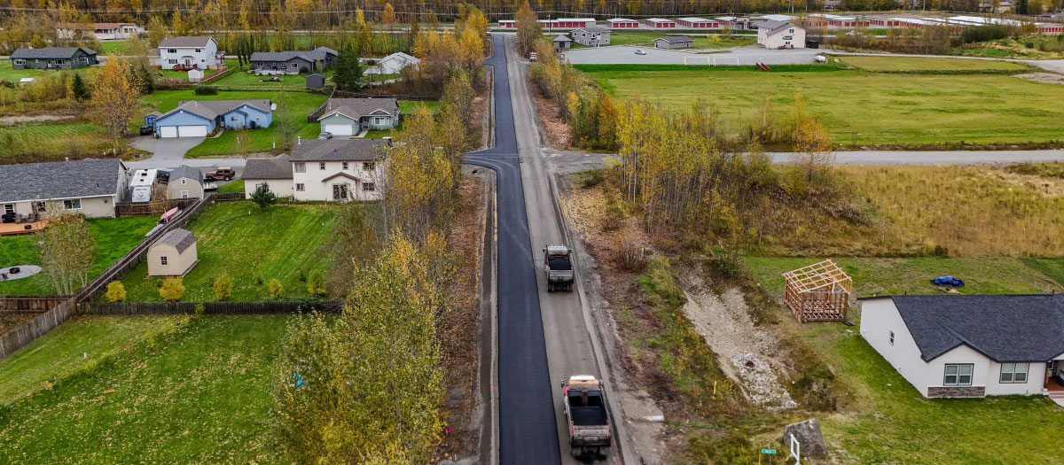 long straight road in between grassy fields