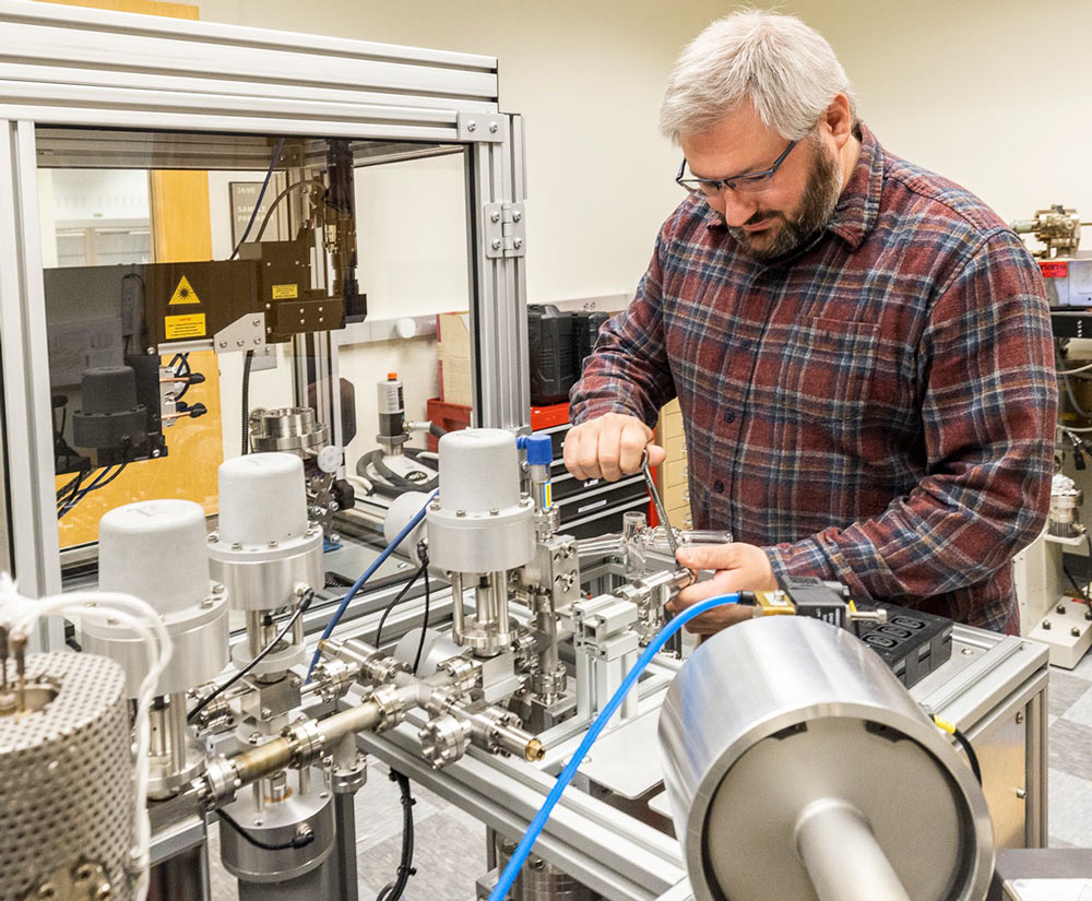 A man in a plaid shirt and glasses works on scientific equipment.
