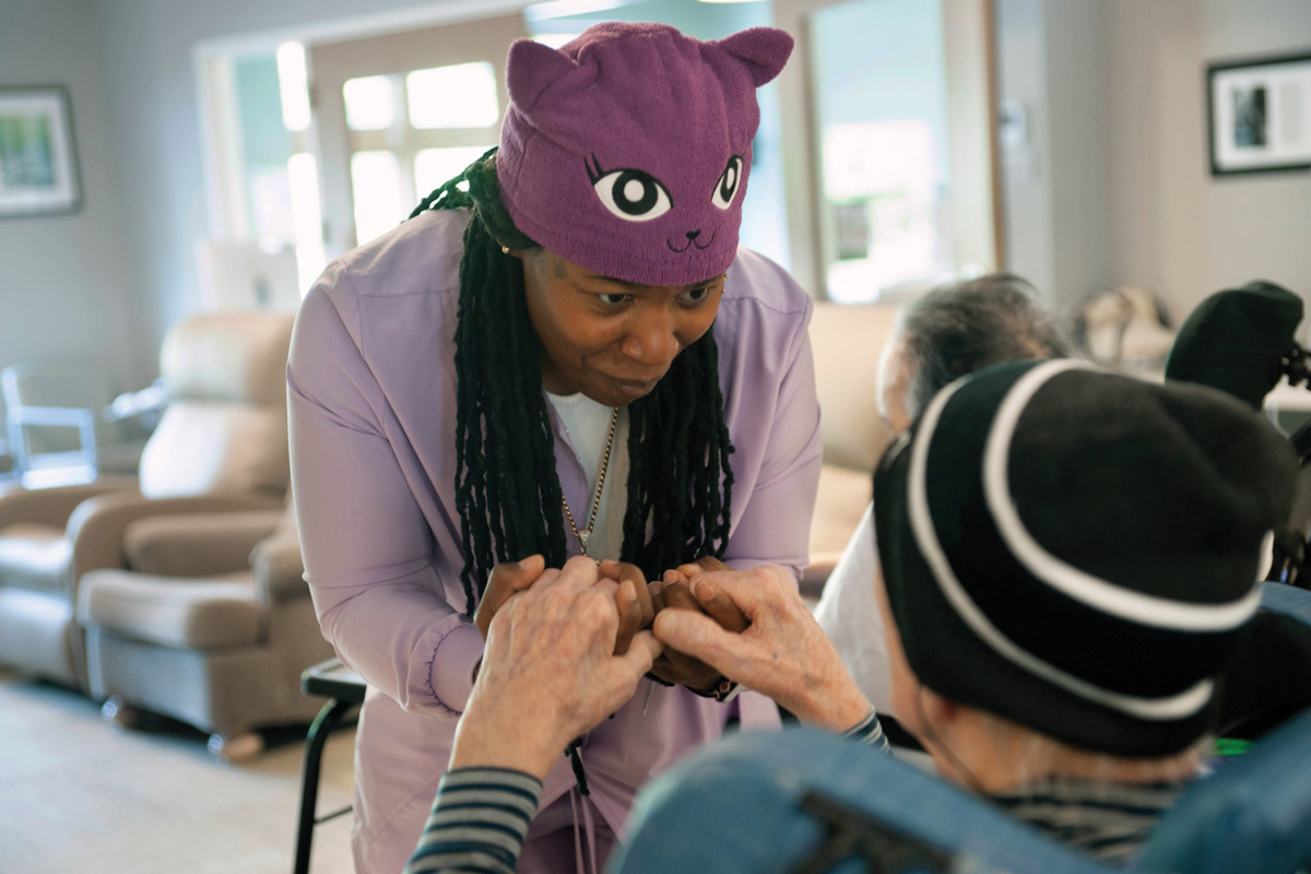 Person in a purple cat hat leans forward, holding hands with a seated individual.