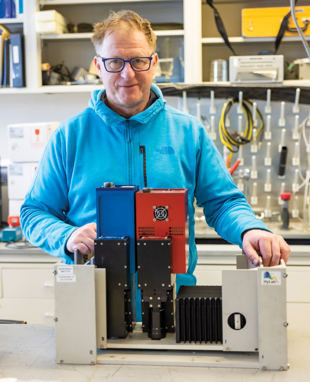 A person in a blue jacket with rectangular lab equipment in front of them.