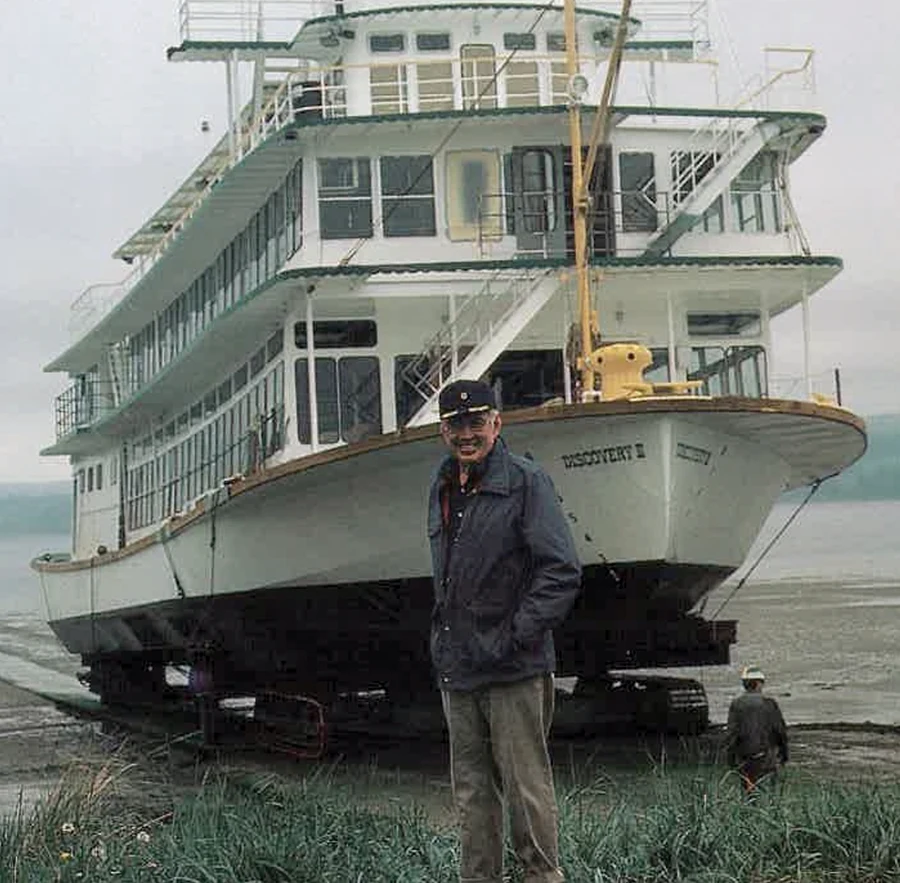 man smiling in front of a steamship on shore