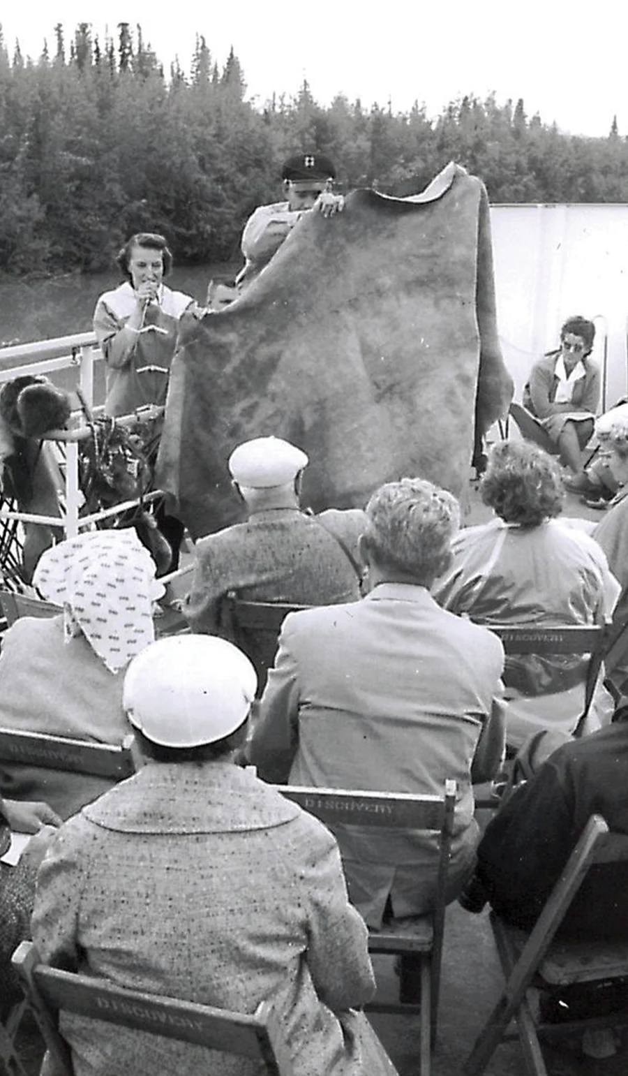 black and white photo of a tour guide holding up a cloth to an audience
