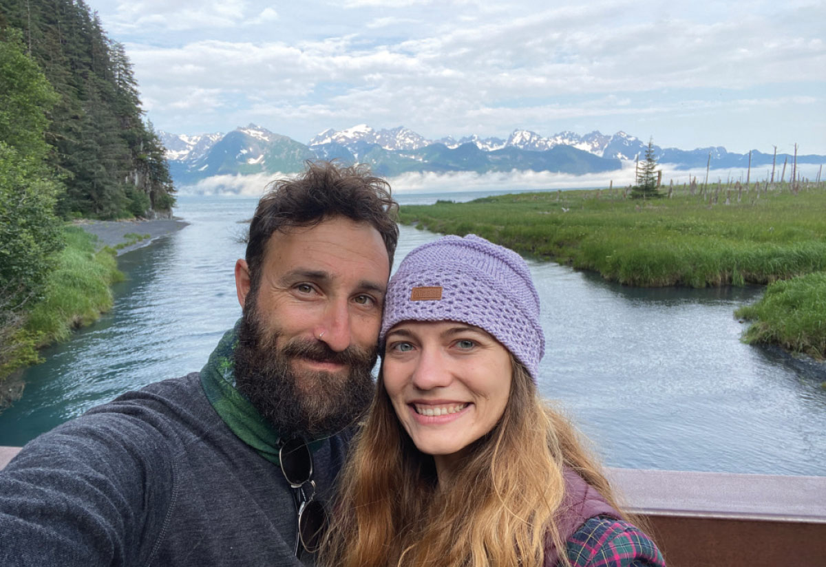 Jared and Ashley Sternberg taking a photo of themselves with a scenic view of greenery and a body of water behind them