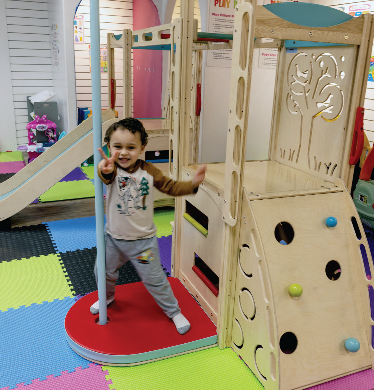 young child doing a peace sign while standing next to play set at Play Palace