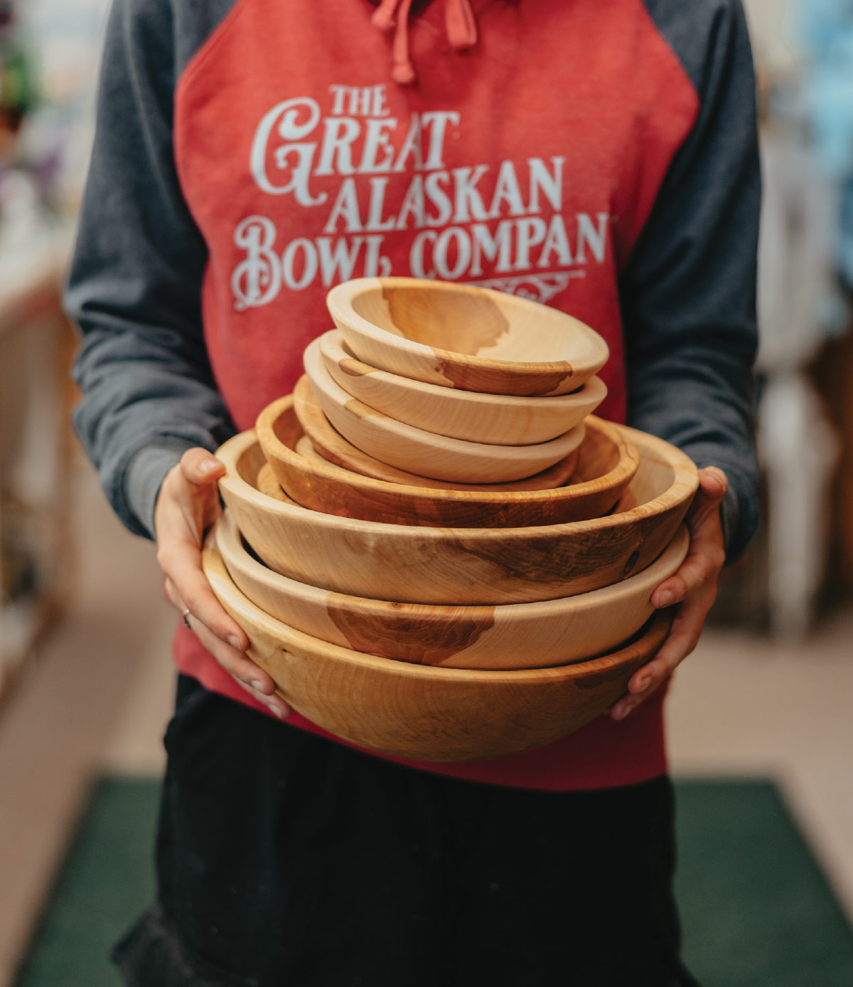 A front-facing, medium close-up shot of a person holding a stack of wooden bowls.