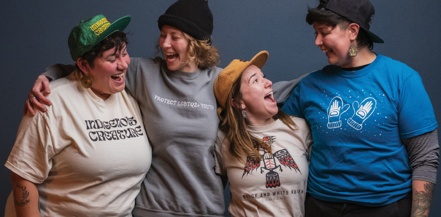 A group portrait shows four people, all women, standing in a line with their arms around each other's shoulders. They are all laughing and smiling.