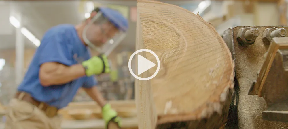 screen capture from a video of a woodworker wearing a face shield and gloves while operating a lathe, shaping a large piece of wood