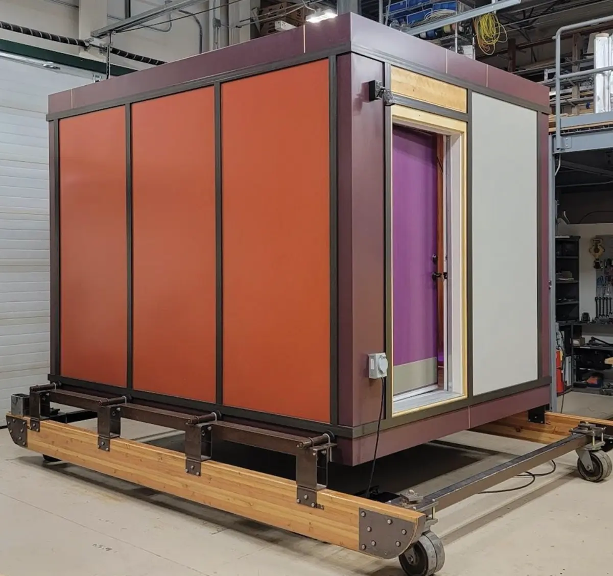 A completed, multi-colored modular housing unit on a wheeled base, inside a workshop.