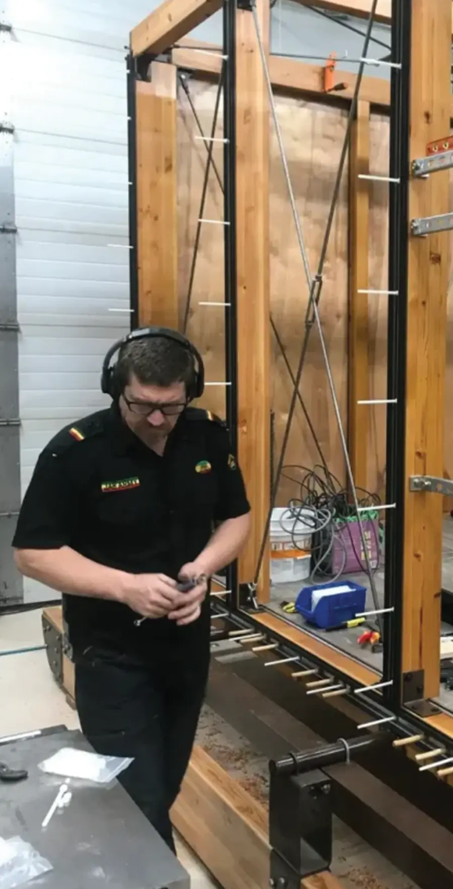 A man in a black uniform and headphones working on a large wooden frame with tension wires and cables.