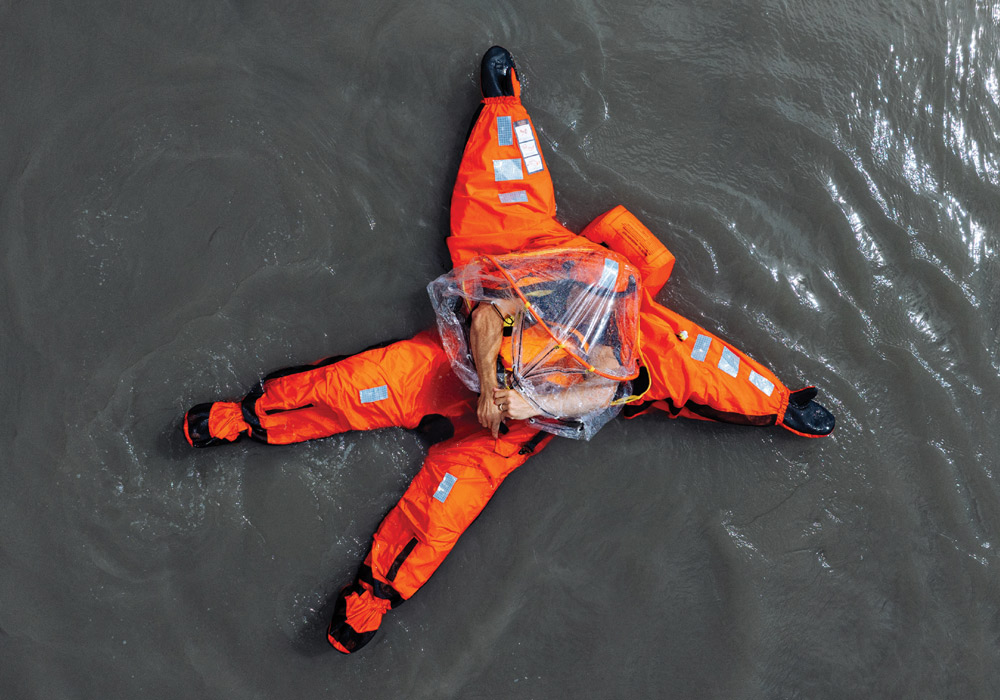 Person in an orange survival suit floating on water.