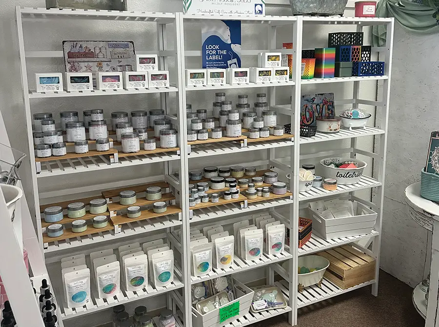 A retail display with several tall, white slatted shelves. The shelves are filled with small jars, tins, and bags of bath and body products, including bath salts, soaps, and lotions.