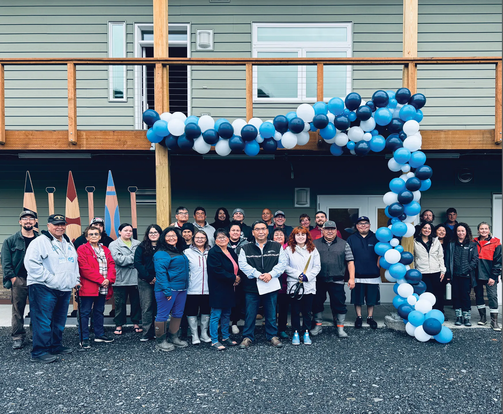 Group of people posing in front of a building decorated with blue, white, and black balloons, with paddles in the background.