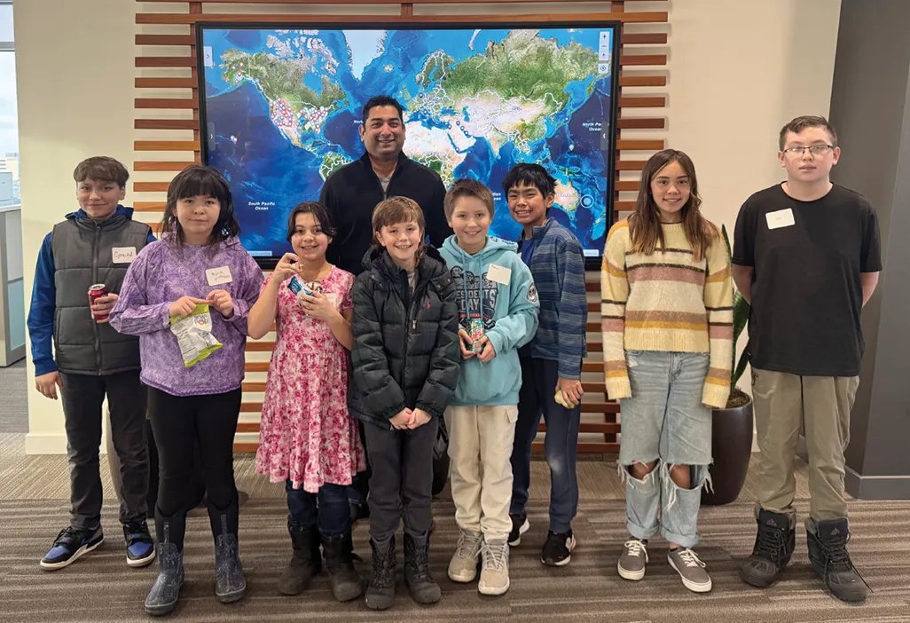 Group of children and an adult posing in front of a large world map display.