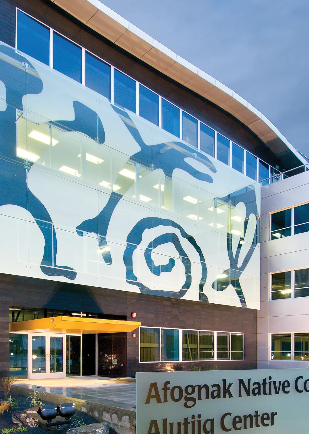 Modern building facade featuring large abstract animal and spiral designs, with a sign for Afognak Native Corporation Alutiiq