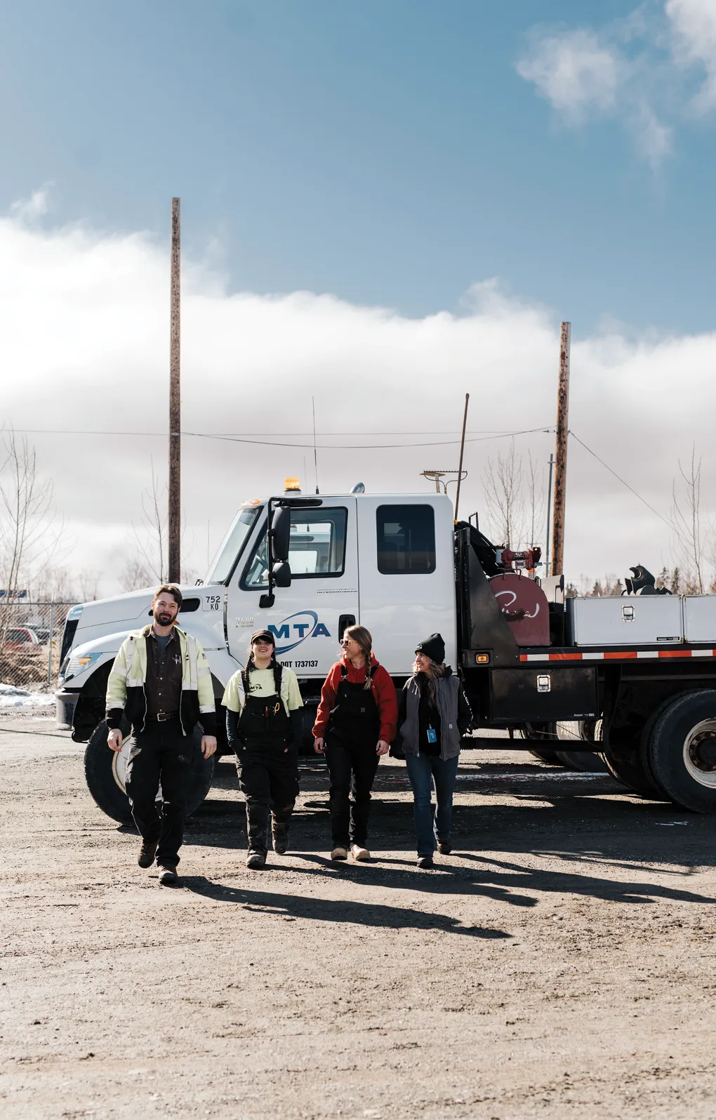 Four people walking towards the camera in front of a large truck with "MTA" logo on a clear day.