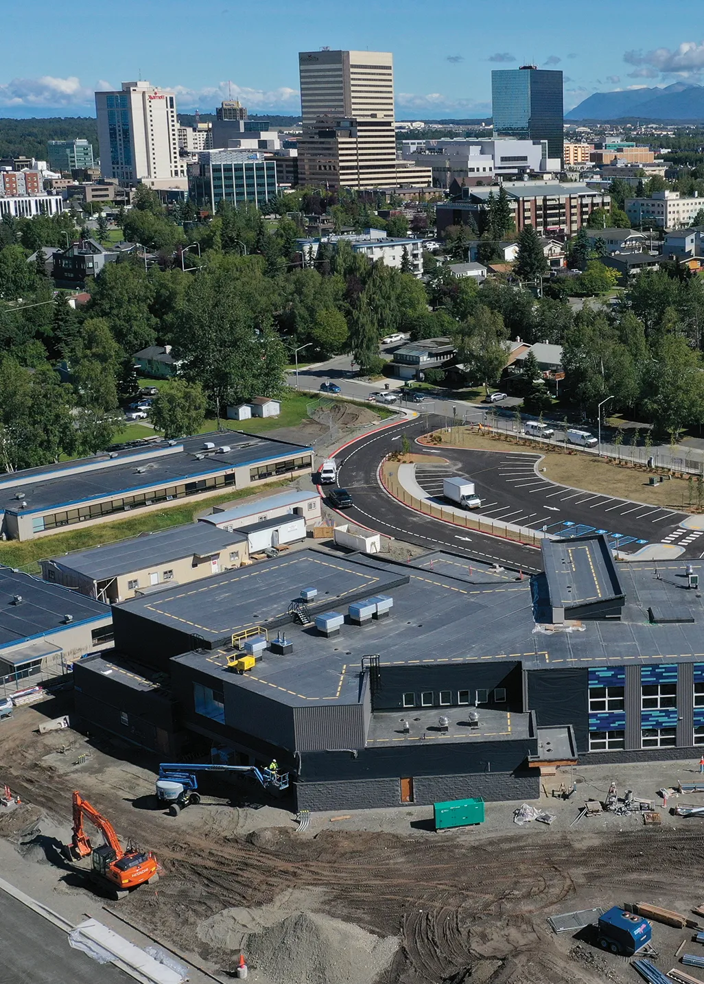 Aerial view of a construction site with buildings, trees, and a city skyline in the background.