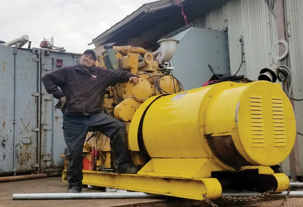 Man posing next to a large yellow generator in an industrial setting.
