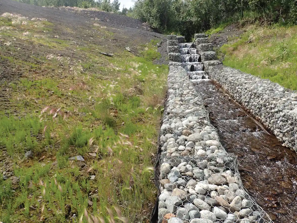 Stepped waterway and banks reinforced with wire-caged river rocks (gabions) next to a hillside with new green growth