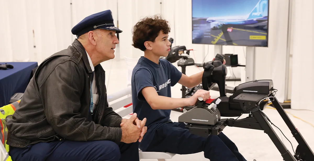 Airline pilot or aviation mentor helping a student use a flight simulator joystick and throttle during an educational event