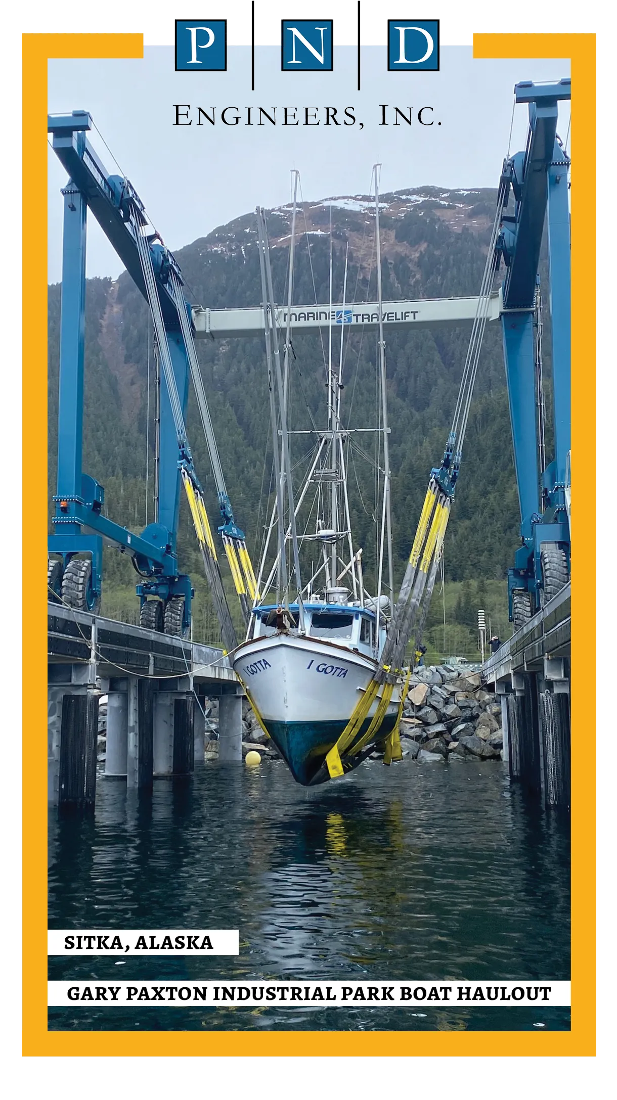 A fishing boat named “I Gotta” is lifted from the water by a large blue Marine Travelift at the Gary Paxton Industrial Park boat haulout in Sitka, Alaska. The scene is framed by yellow border accents with the logo “PND Engineers, Inc.” above. Snow-dusted mountains and evergreen trees rise in the background under an overcast sky.
