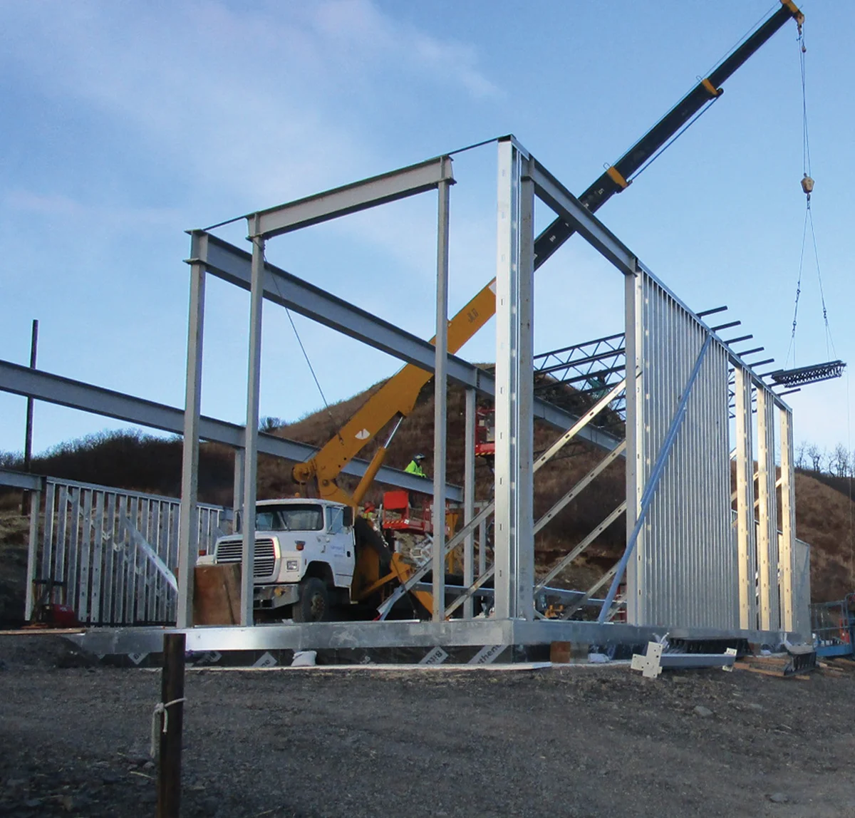 Construction site in Alaska showing the steel frame erection of a commercial building, with a crane and heavy equipment nearby