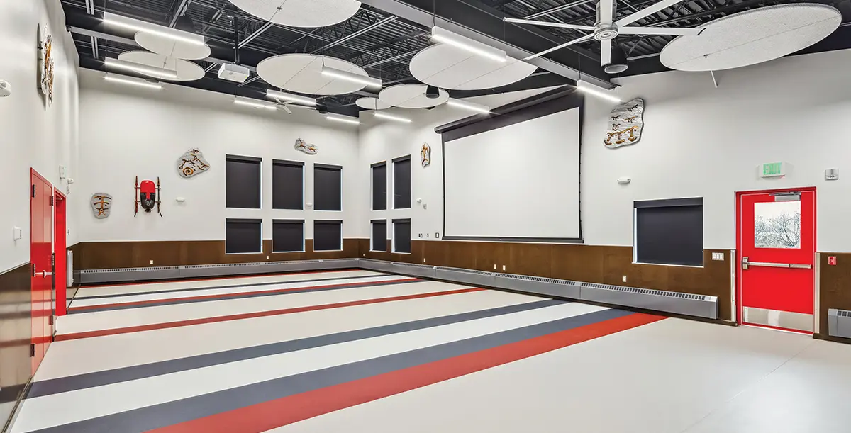 Interior of a new community center multipurpose room with a projector screen, painted floor stripes, and cultural decorations on the walls
