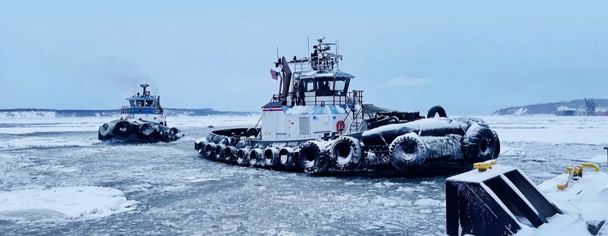 Two powerful ice-breaking tugboats navigating through thick ice floes in Cook Inlet, Alaska, during winter conditions.