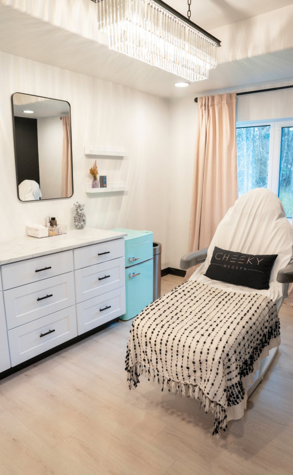 A clean, modern medical spa treatment room featuring a white reclining chair, a marble-topped vanity, and a small mint-green refrigerator.