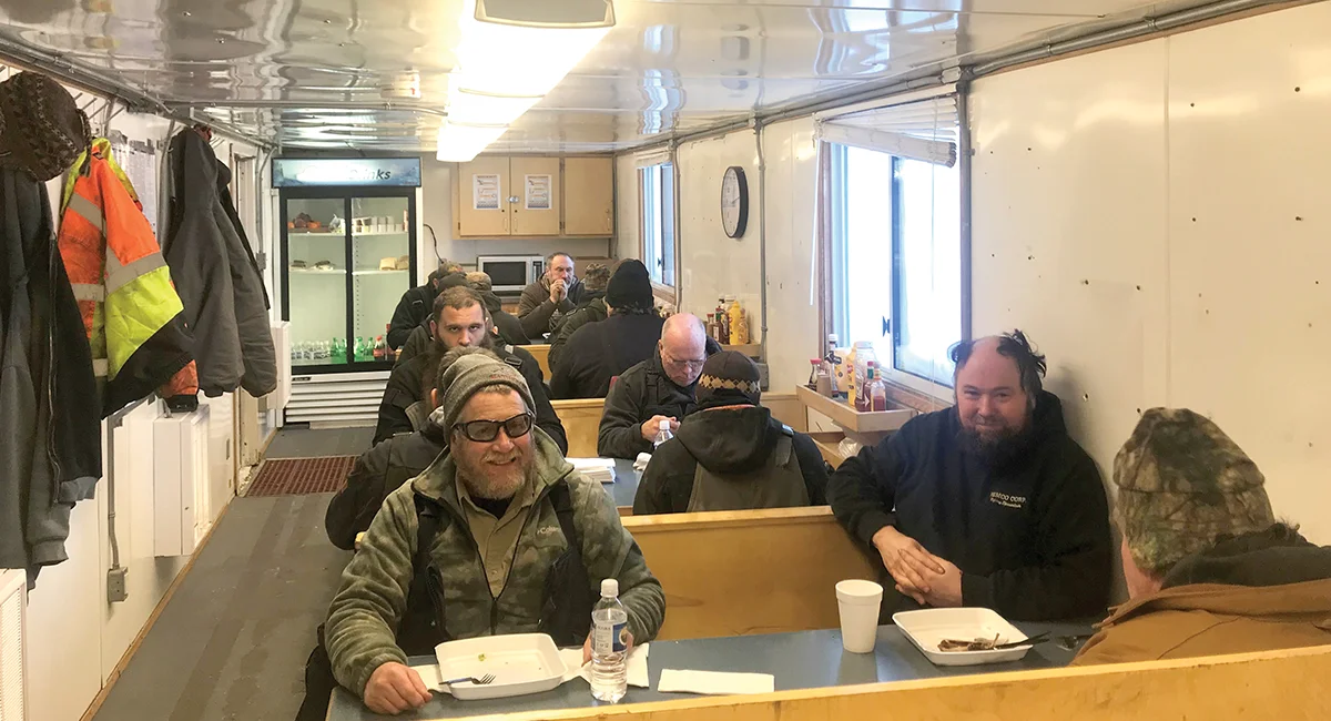 Interior of a remote workforce dining hall featuring booth seating, a refrigerator, and workers in cold-weather gear.