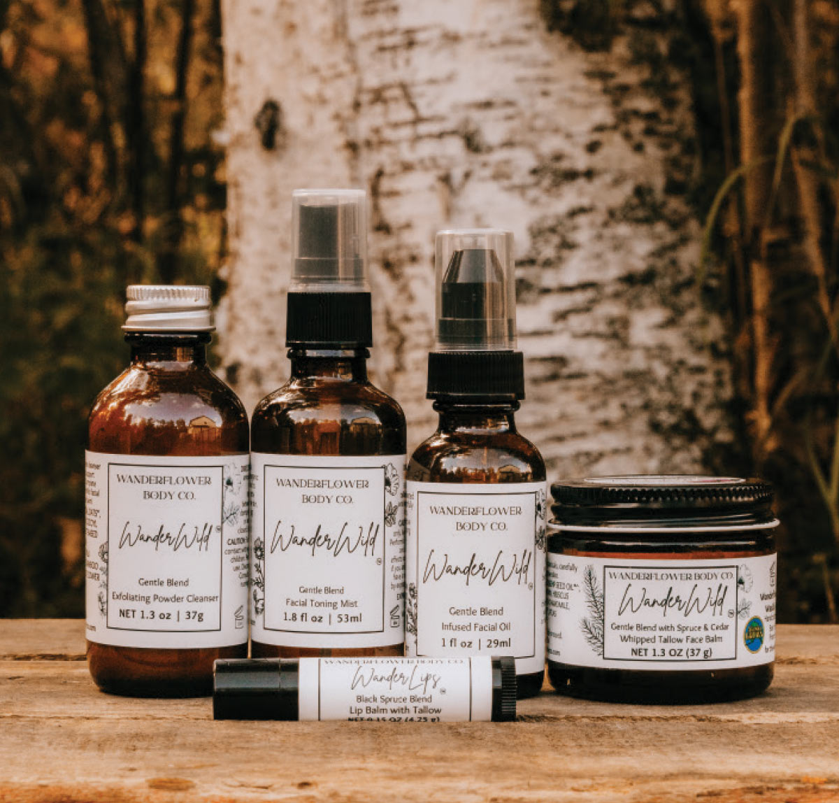 A collection of brown glass bottles and jars from Wanderflower Body Co., including facial mists and balms, displayed on a wooden surface.