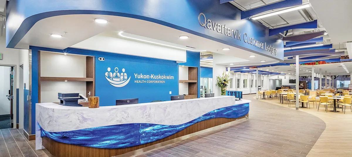 Modern hospital cafeteria and dining hall featuring light wood seating, contemporary pendant lighting, and a vibrant wall mural depicting nature and agriculture scenes