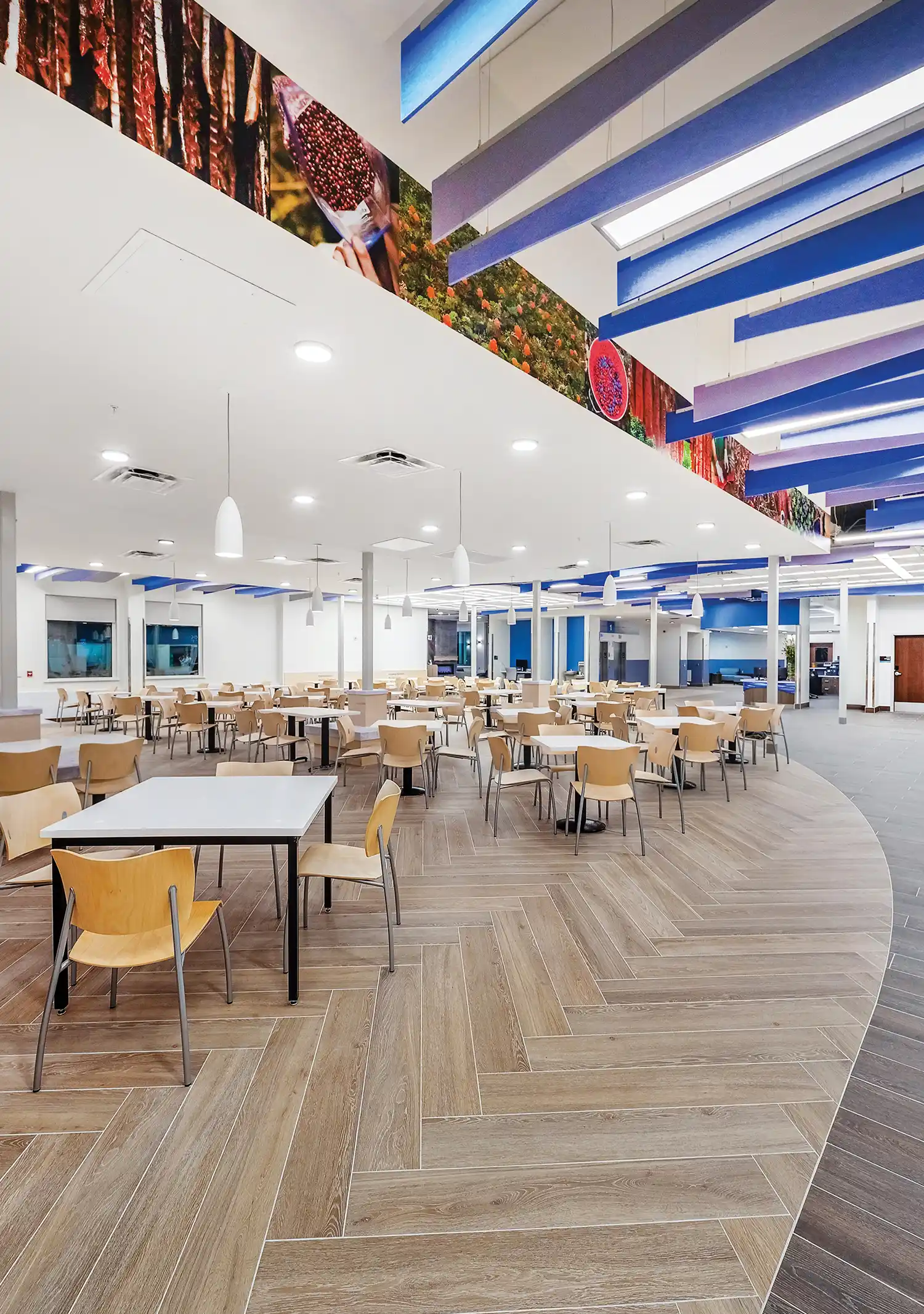 A bright, open-concept dining hall with contemporary pendant lighting, vibrant nature murals, and integrated architectural elements designed for patient and staff wellness