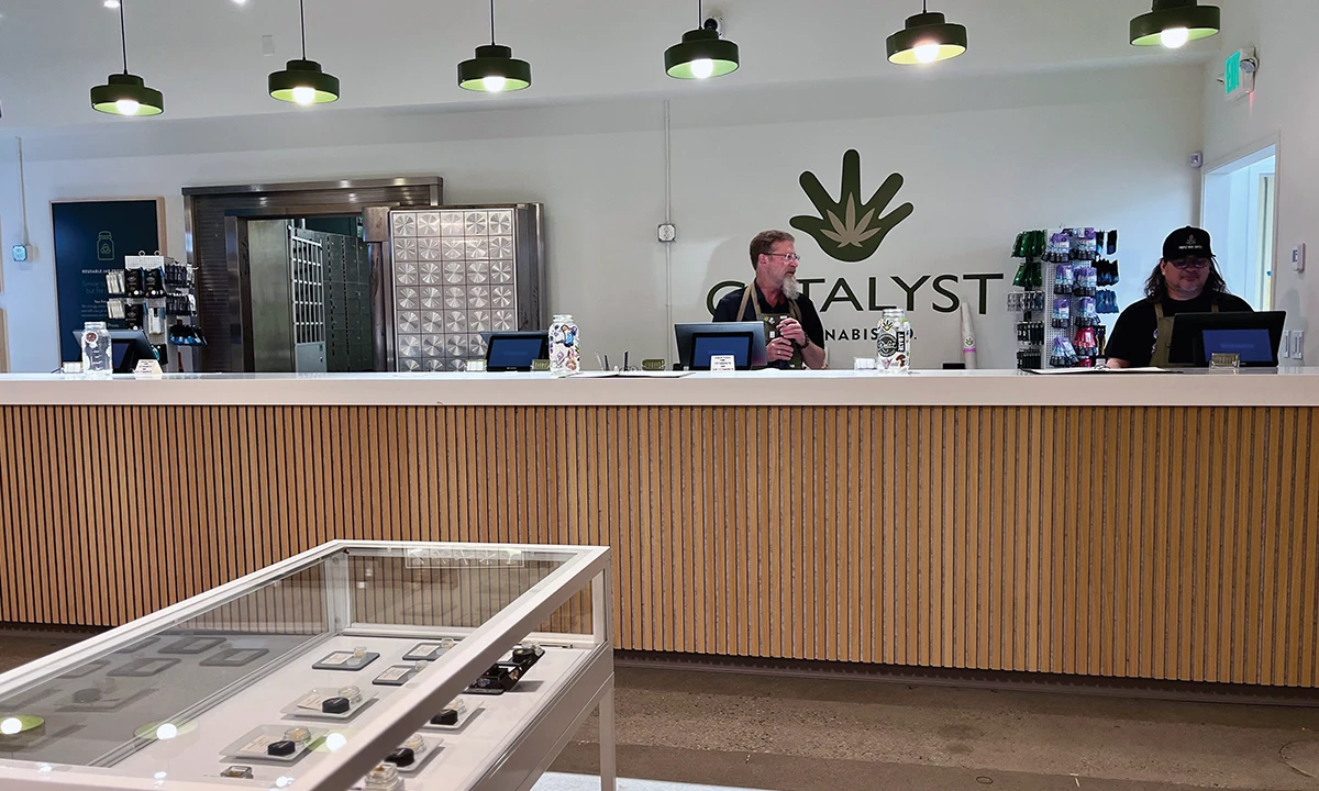 Interior view of Catalyst Cannabis Co. in Alaska, featuring a long wood-paneled service counter, glass display cases, and professional staff behind the register.