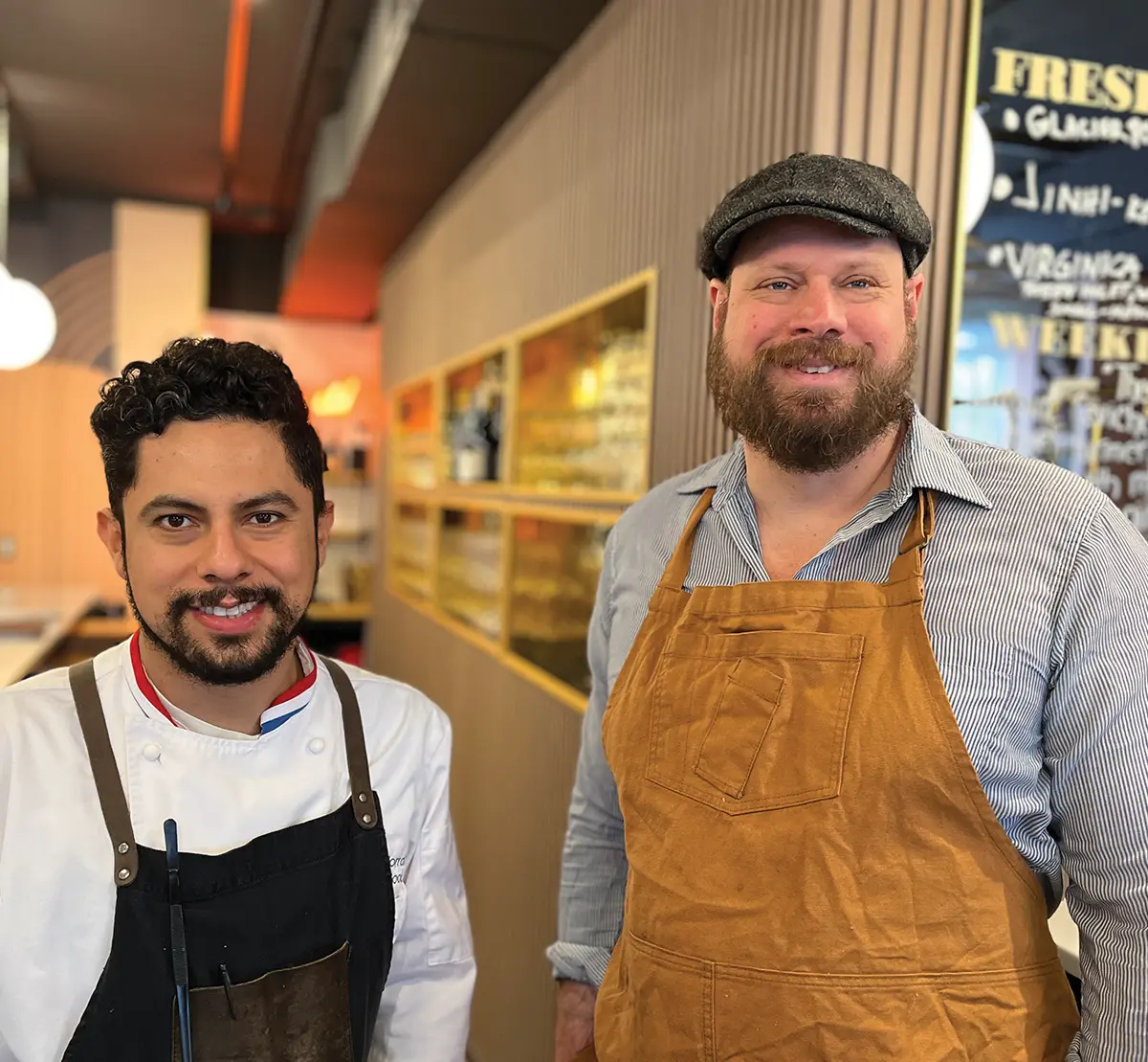 Chefs from a local Alaskan eatery posing in a stylish dining room with vertical wood paneling and a menu board in the background.