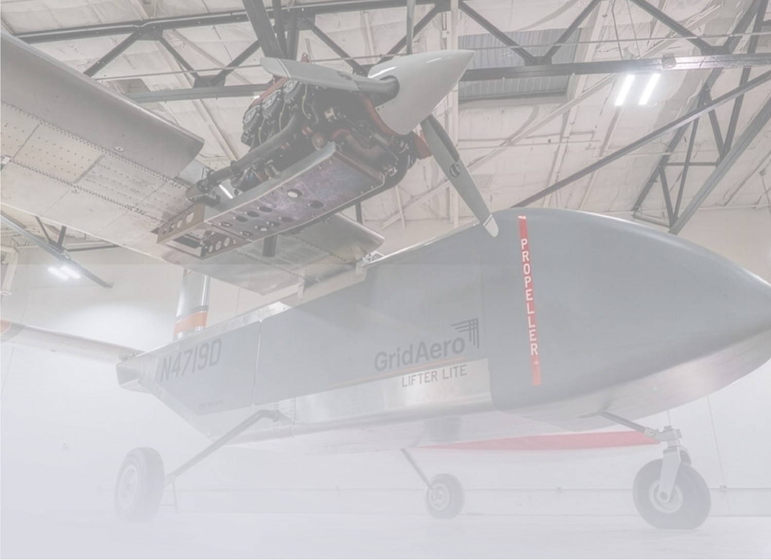 A grey GridAero Lifter Lite drone with a front-mounted propeller parked inside a bright, high-ceilinged aircraft hangar.