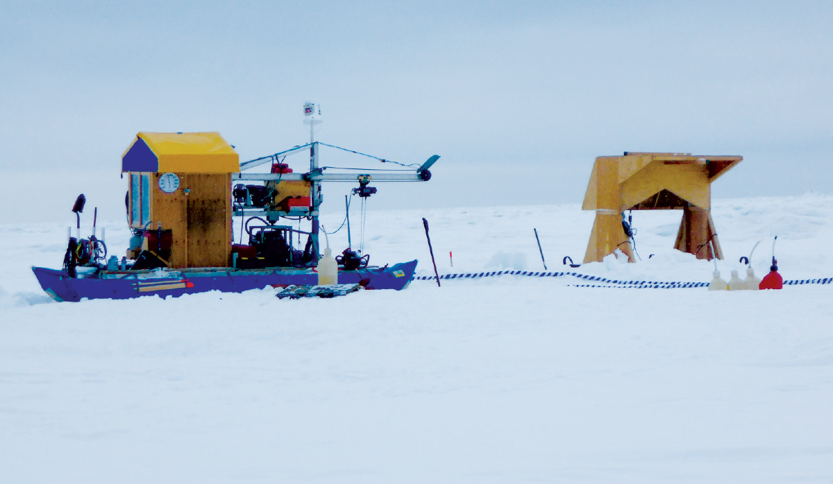 A small blue mining boat and a yellow wooden structure positioned on a vast, flat expanse of white snow and ice.