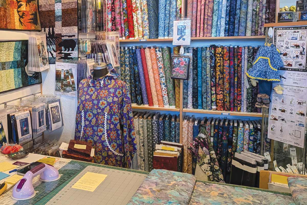 Interior of a craft shop showing walls of fabric bolts, patterns, and a mannequin wearing a colorful floral garment.