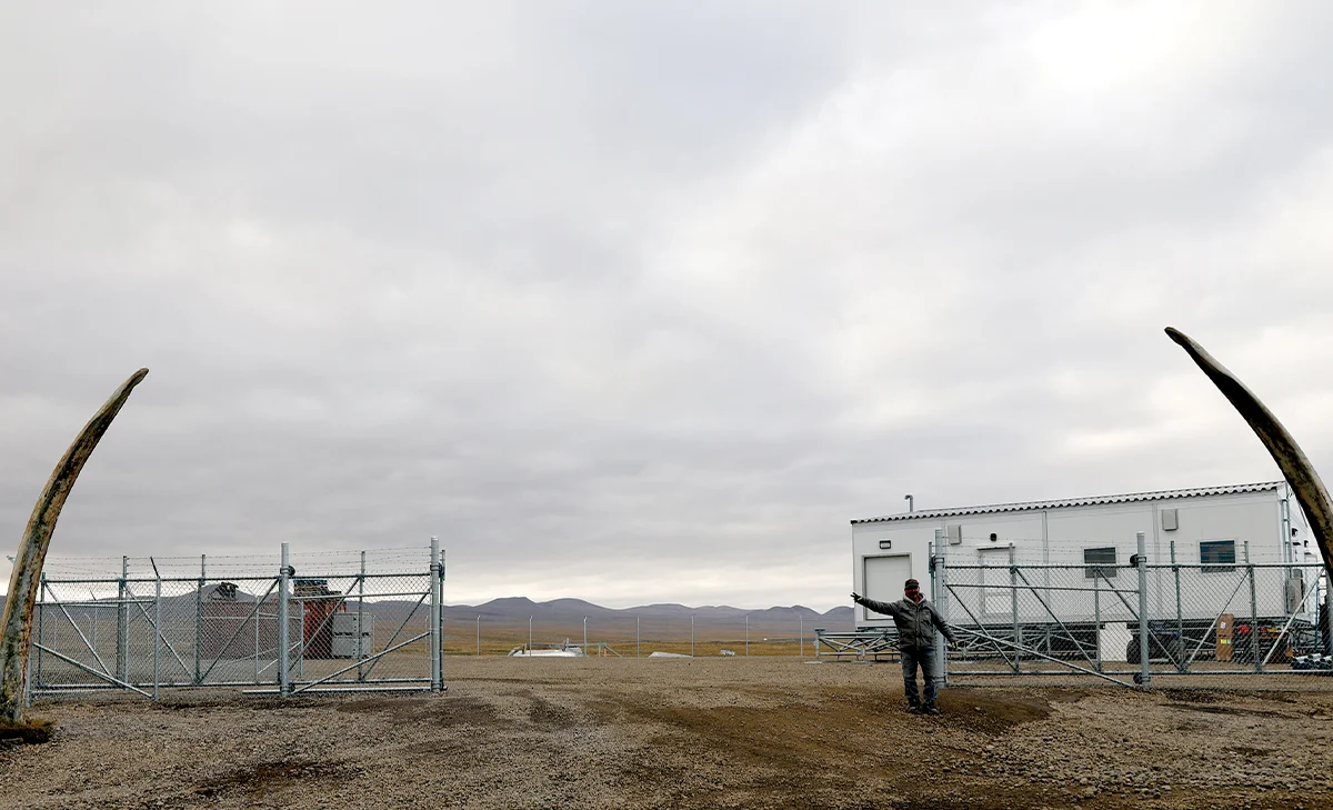 A modular meat processing facility in a remote Alaskan community, featuring white industrial units elevated on steel space-frame foundations with a person gesturing toward the entrance