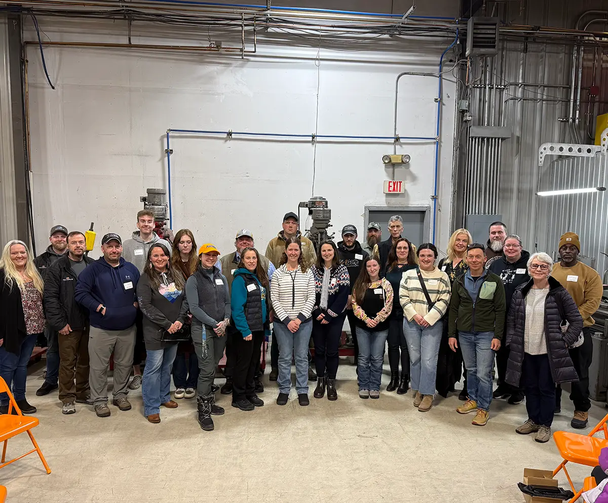 A large group of people posing for a group photo inside an industrial warehouse or workshop facility