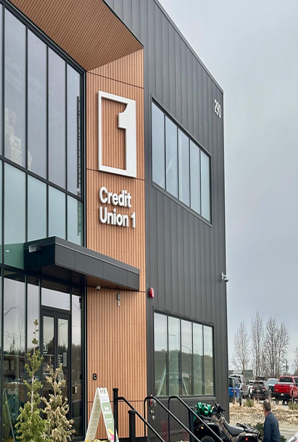 The modern exterior of a Credit Union 1 branch, featuring dark metal siding and a vertical light-wood-paneled entrance section.