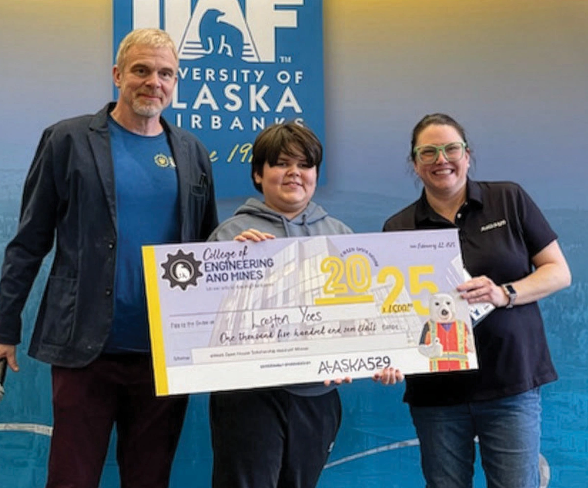 Two adults and a youth hold a large $1,500 ceremonial check in front of a University of Alaska Fairbanks backdrop. The check is awarded to Laughton Yoes for the Engineering Open House Scholarship and is sponsored by Alaska 529.