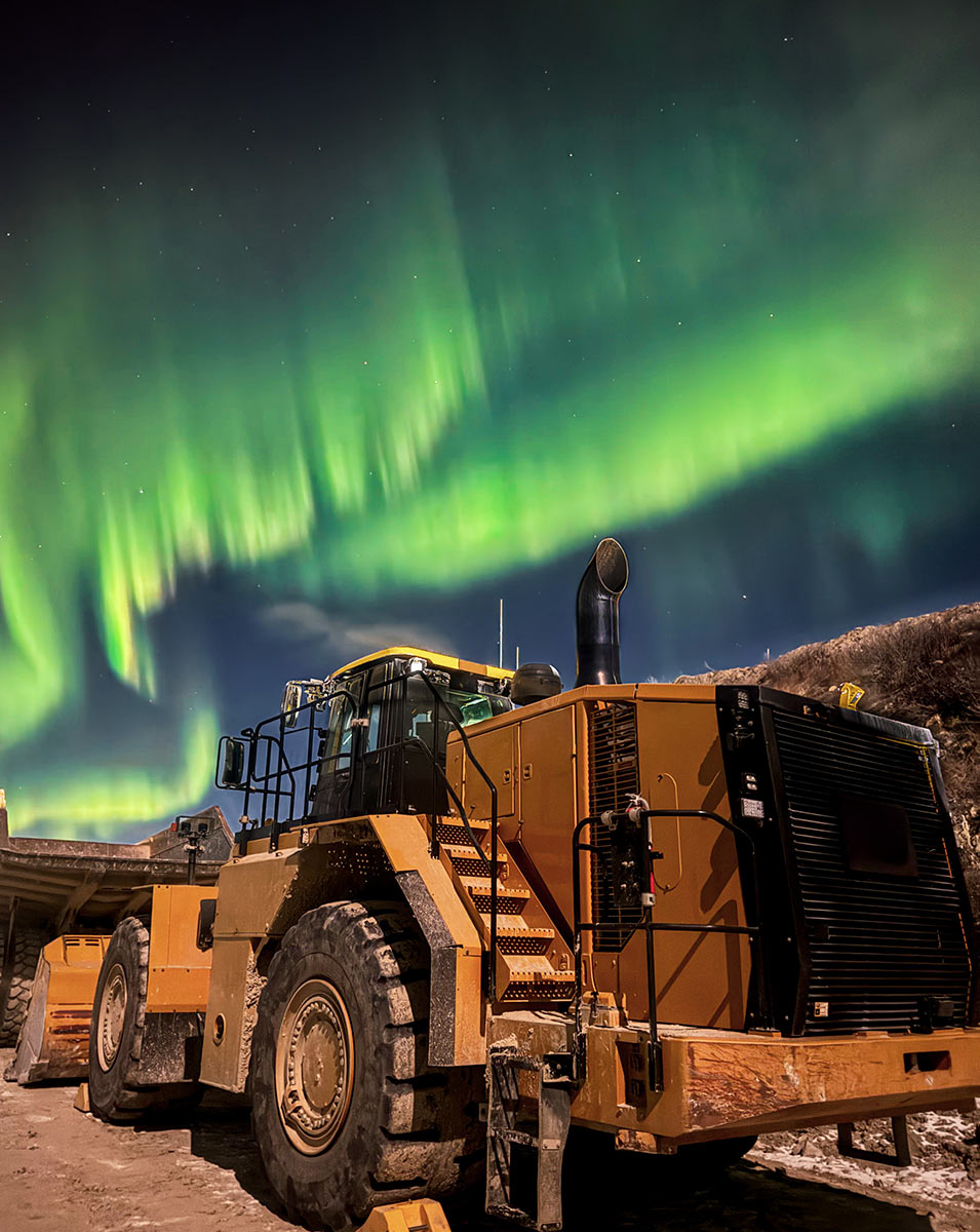 updward angled view of a large yellow tractor under vibrant green northern lights