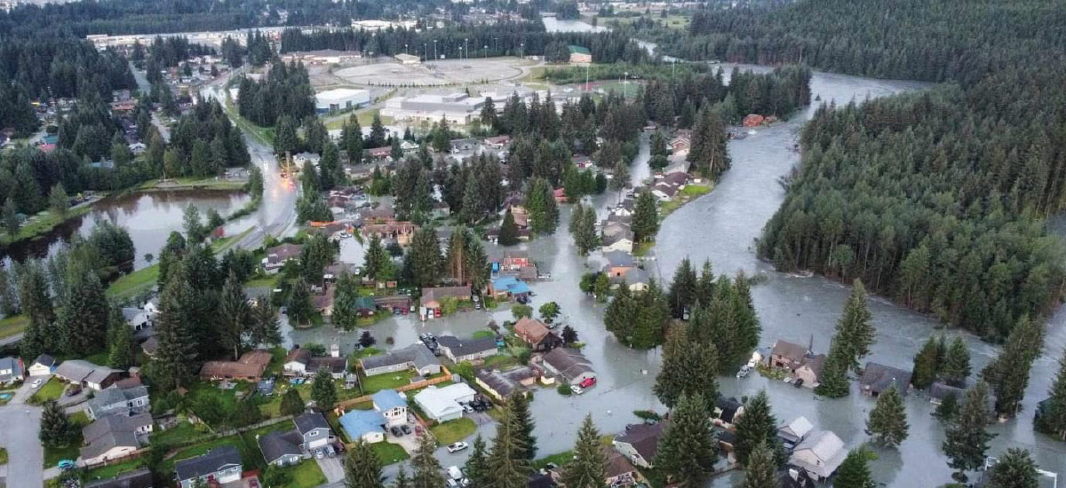 An aerial view of a residential neighborhood experiencing significant flooding, with water surrounding houses and flowing through the streets.