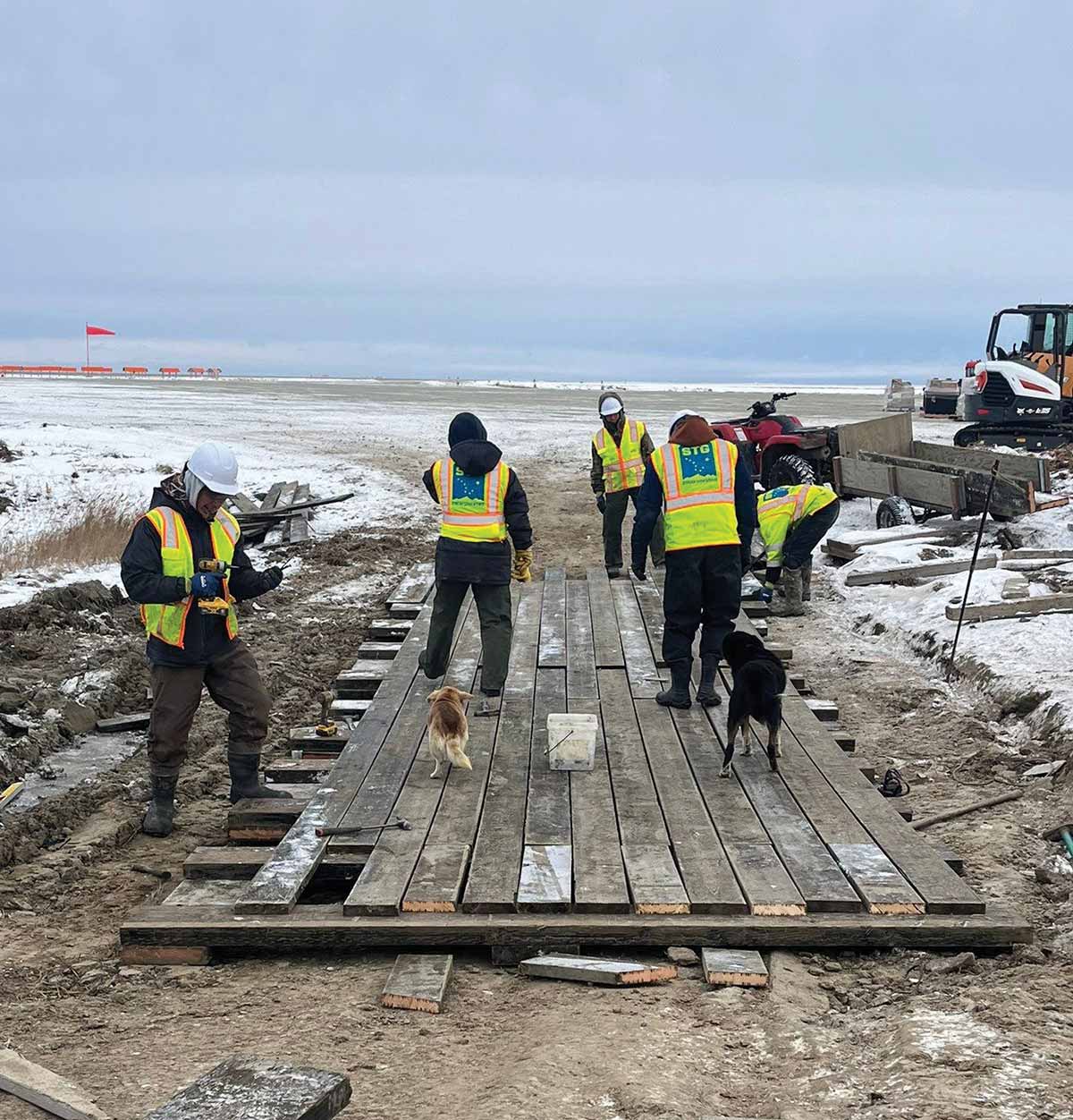 Construction crew in high-visibility vests building a wooden boardwalk in a snowy landscape.