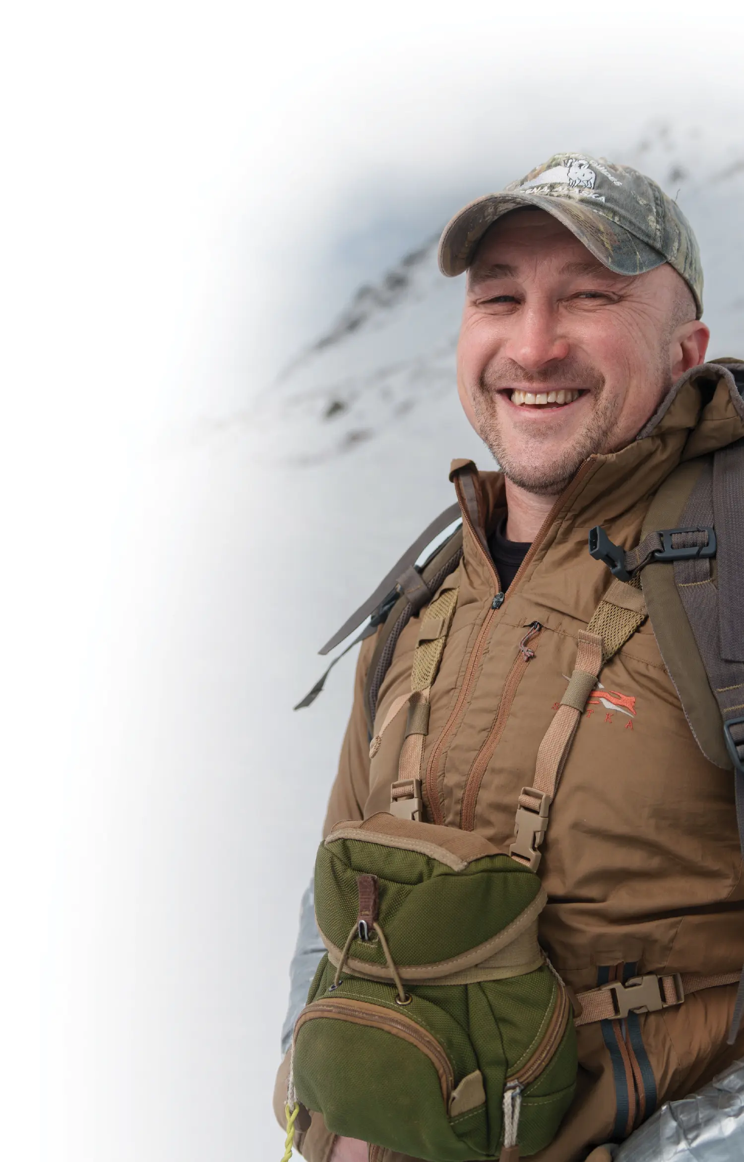 Jeff Miller, a man smiling outfitted in professional hiking outdoor gear attire standing in snow on top of a snowy covered hillside on a cloudy day