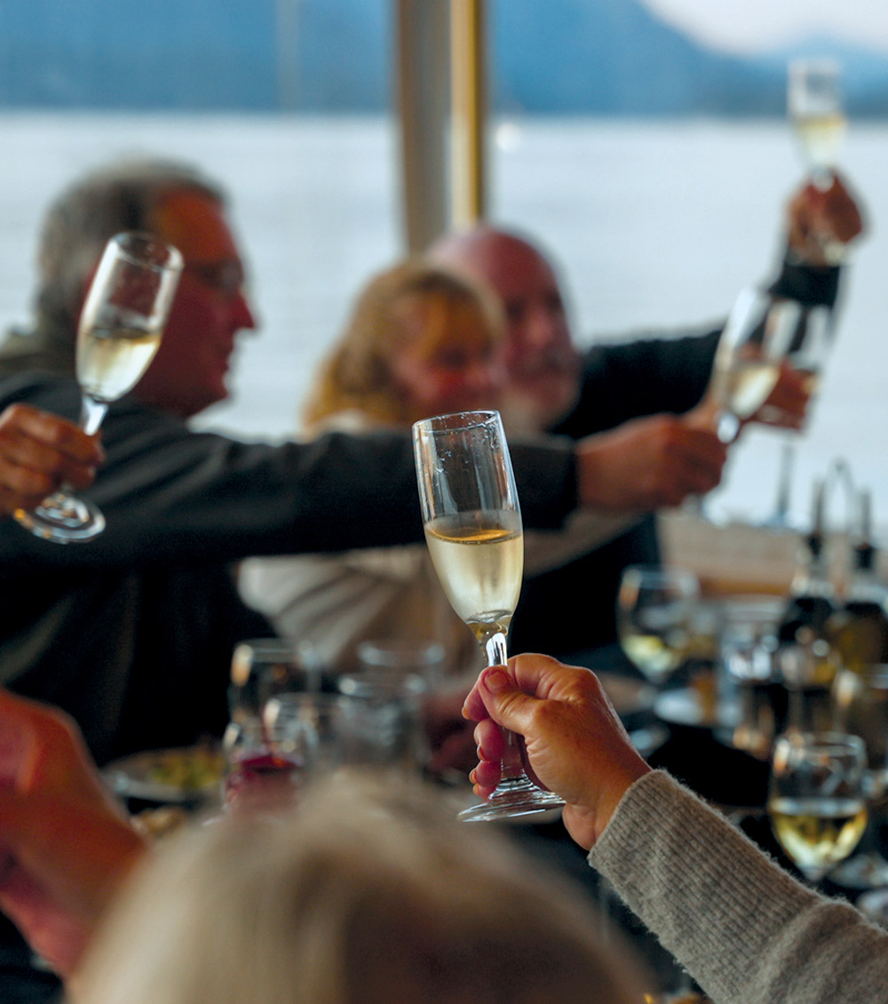 A close-up, shallow-focus shot of several people raising champagne flutes in a toast inside a boat's dining area.